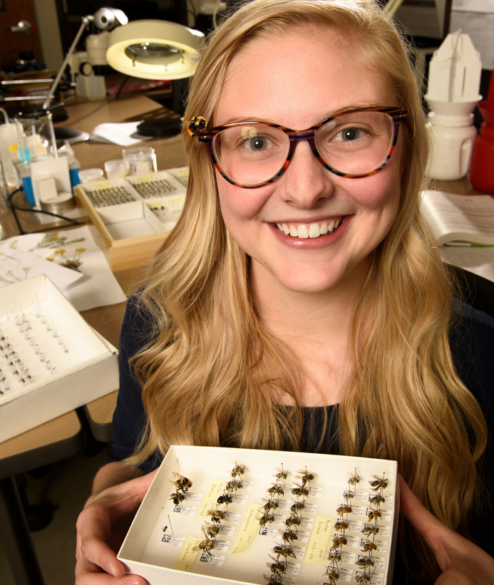 Insect biology student smiling with boxes of insects