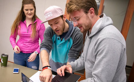 Three students look at a laptop