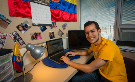 Student smiling for picture in dorm room while working on a laptop