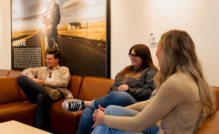 Three students talk to each other while sitting on an orange couch