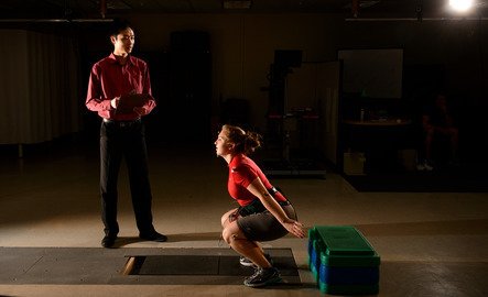Student exercising as kinesiology and health promotion faculty observes