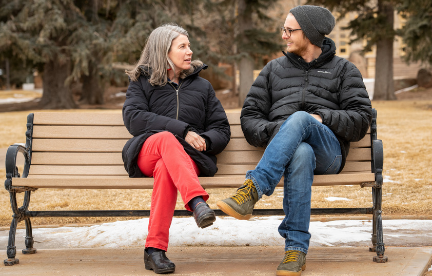 A professor and student talk on a bench on campus