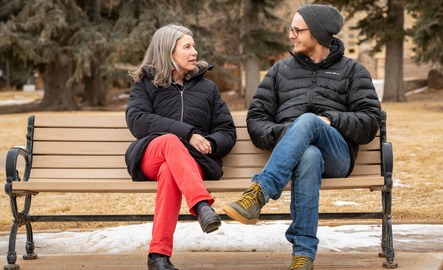 A professor and student talk on a bench on campus