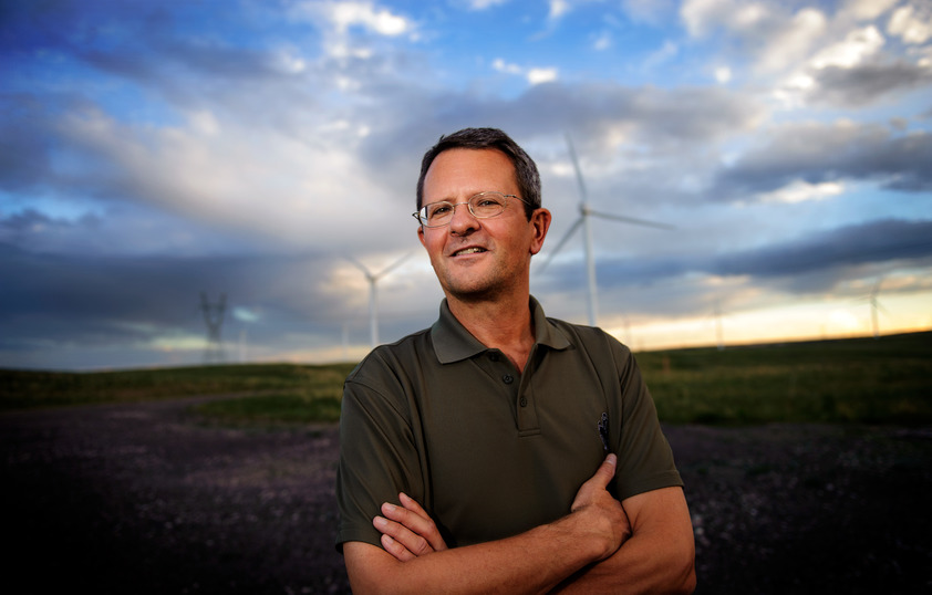 Dr. Stefan Heinz is standing in a field with wind turbines in the distance