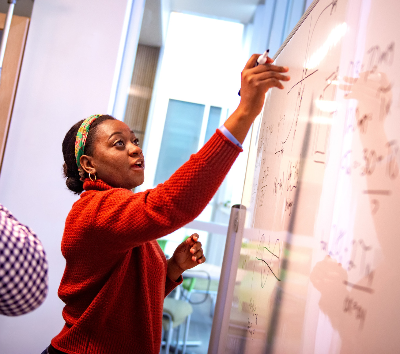 a young Black woman is at a whiteboard working on math equations