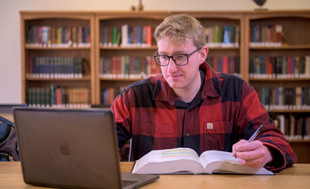A student works on their laptop and an open textbook