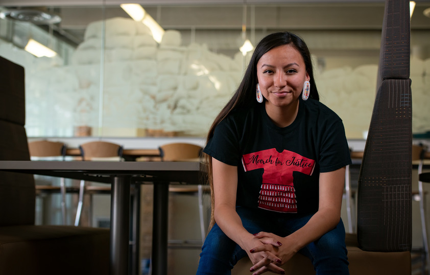 A Native American and Indigenous Studies student is smiling and wearing beaded earrings and a tshirt for the March for Justice