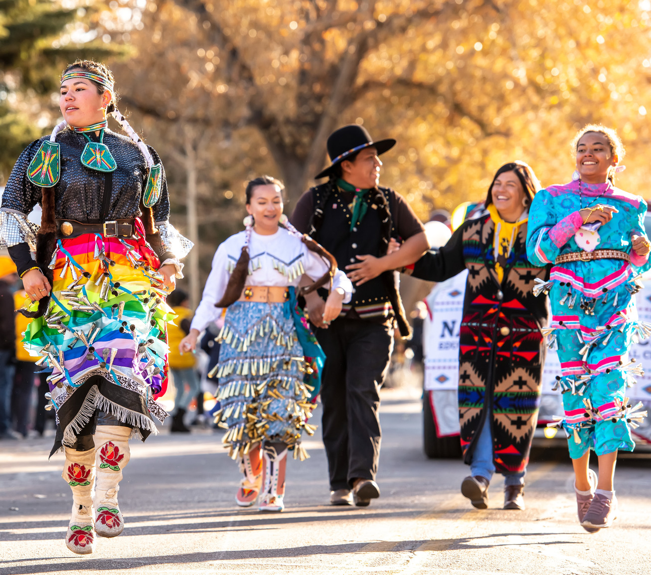 A group of Native American students wearing regalia walk in a homecoming parade