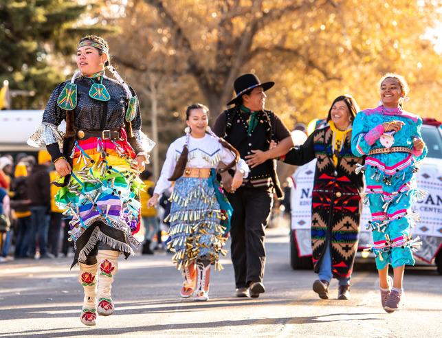 A group of Native American students wearing regalia walk in UW homecoming parade