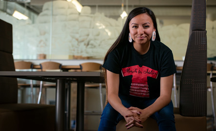 A Native American and Indigenous Studies student is smiling and wearing beaded earrings and a tshirt for the March for Justice