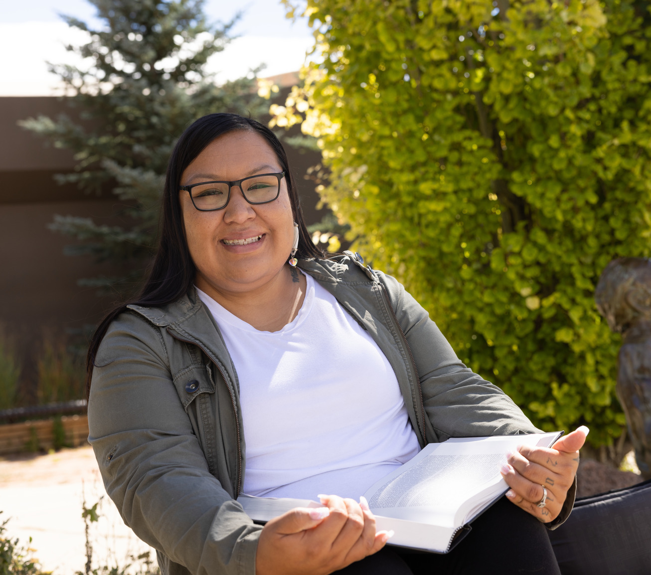 A student smiles for a photo outside while holding open a book
