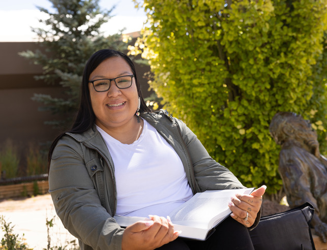 Student smiles while holding a book outside