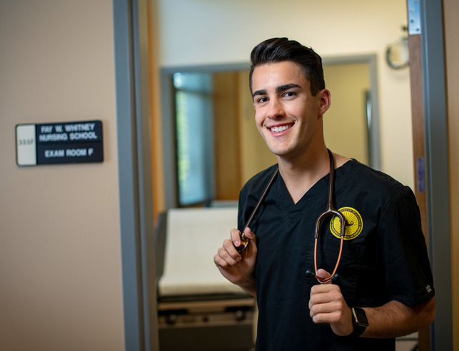 A nursing student stands in the UW nursing building with their stethoscope 