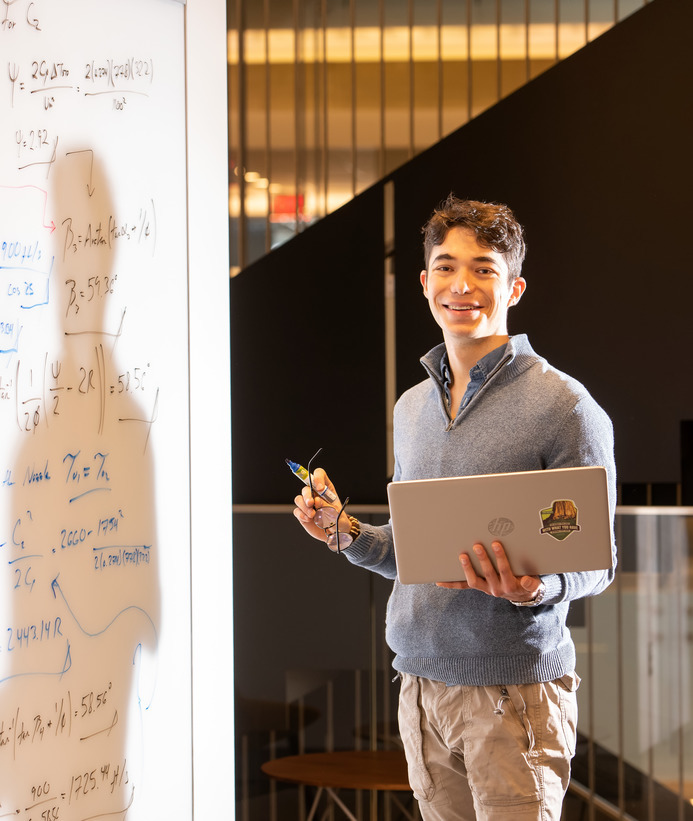 Online instructor holding laptop near whiteboard