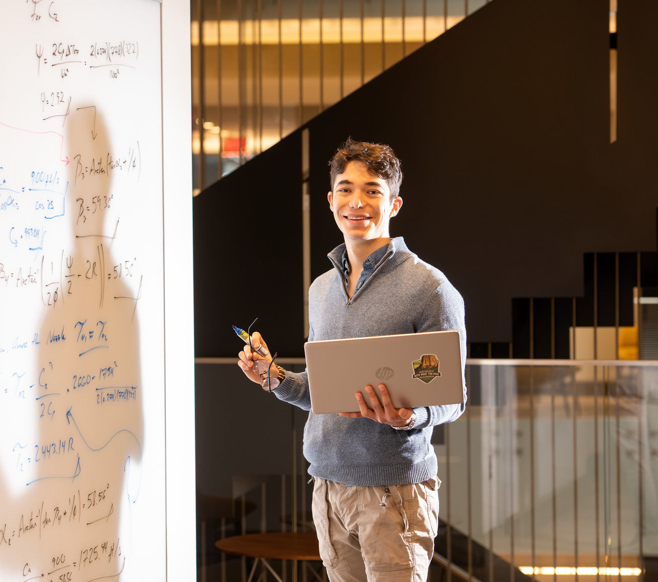 Student holding laptop near whiteboard