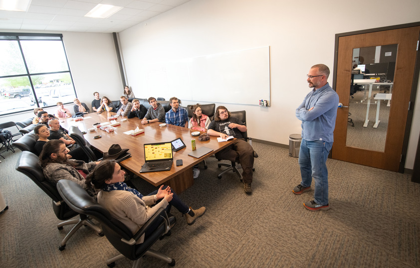 A speaker talks to a group of people sitting at a large conference table during a meeting