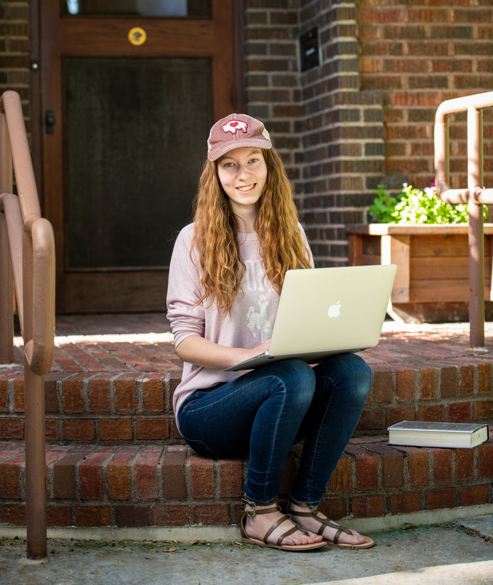 Student sits on the front step of a building on their computer
