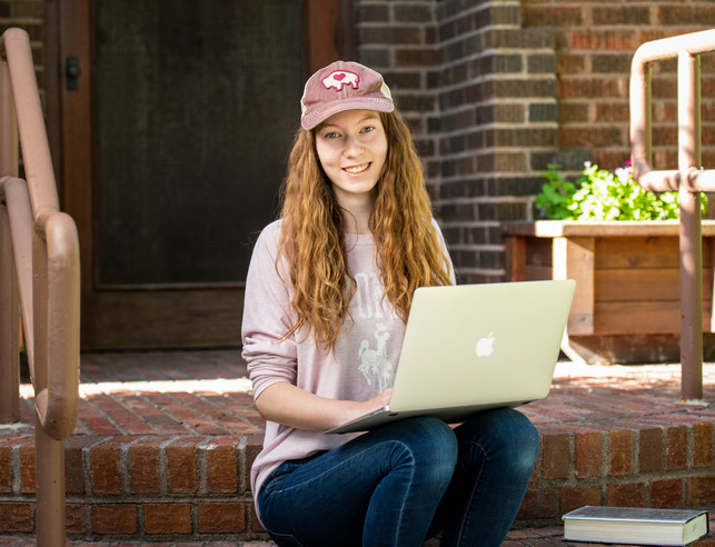 Student sits on the front step of a building on their computer