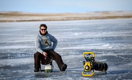 A student ice fishing smiles for a photo