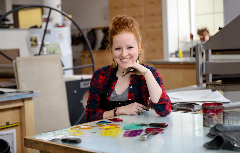 A student smiles for a photo while seated in an art class