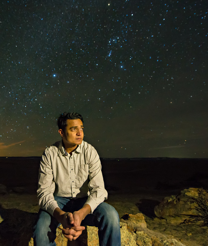 A person looks off into the distance while sitting on a rock