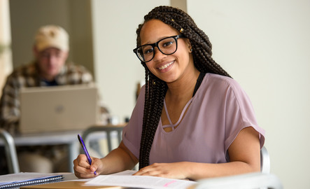 Student smiles at the camera while writing