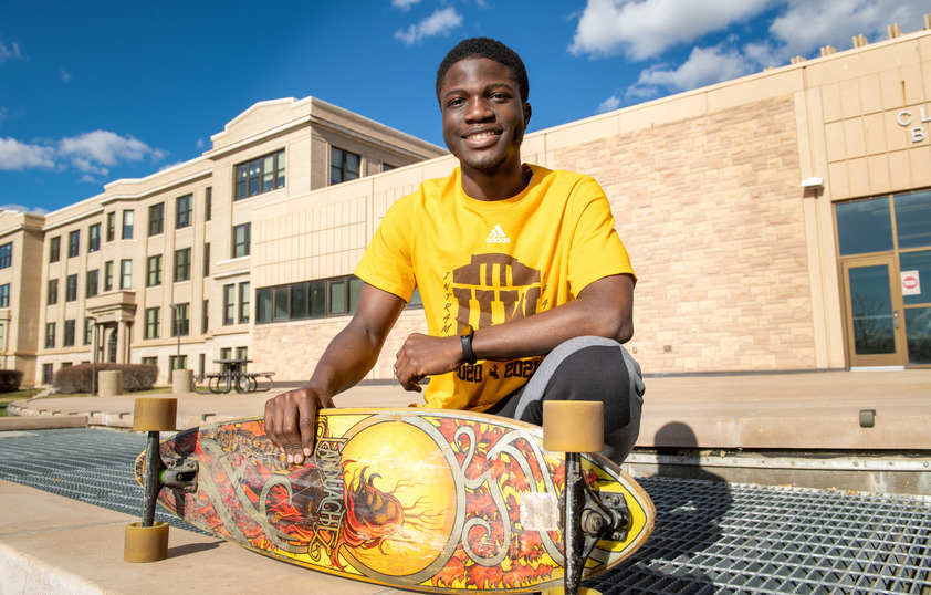 A student smiles for a photo while holding his skateboard