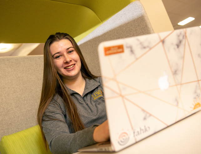 A pharmacy student smiles for a photo while on their laptop
