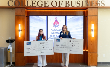 Two sales students hold giant checks