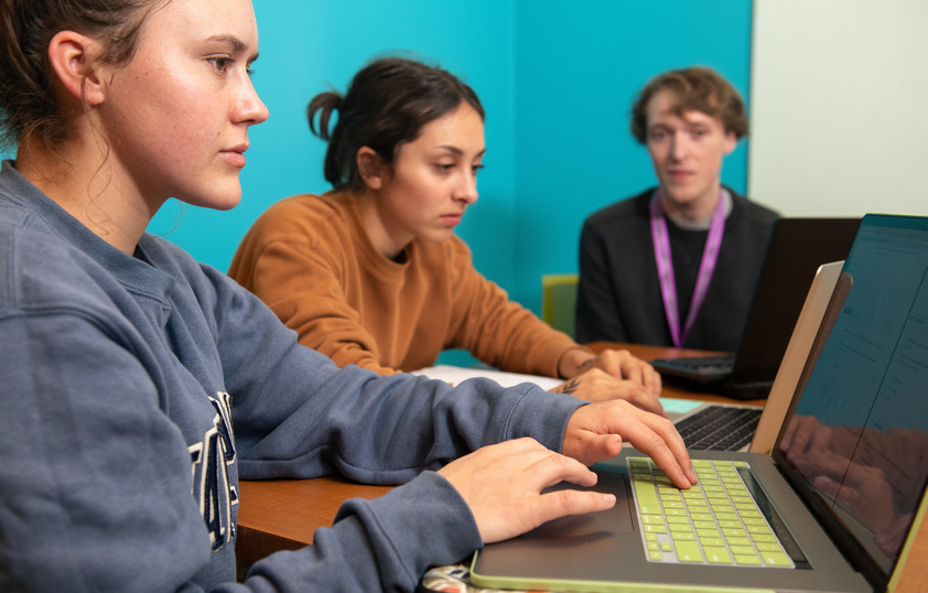 Two students working on their laptops with a tutor