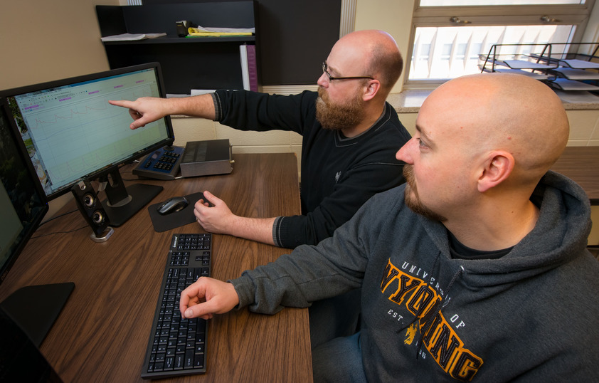 Two people sit and look at computer screens with a graph on it together