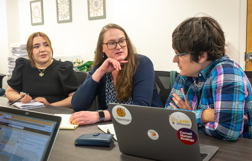 Three people talk at a conference table