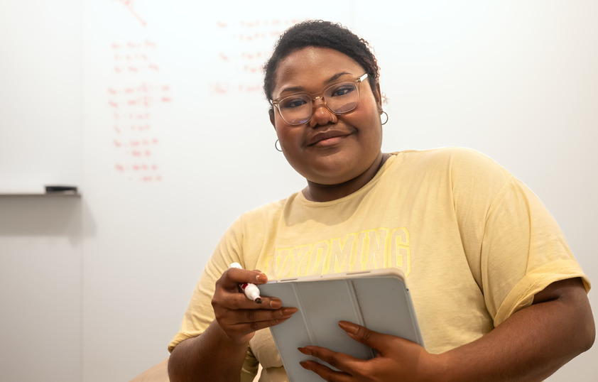 A student smiles for the camera while holding a dry erase market and an ipad