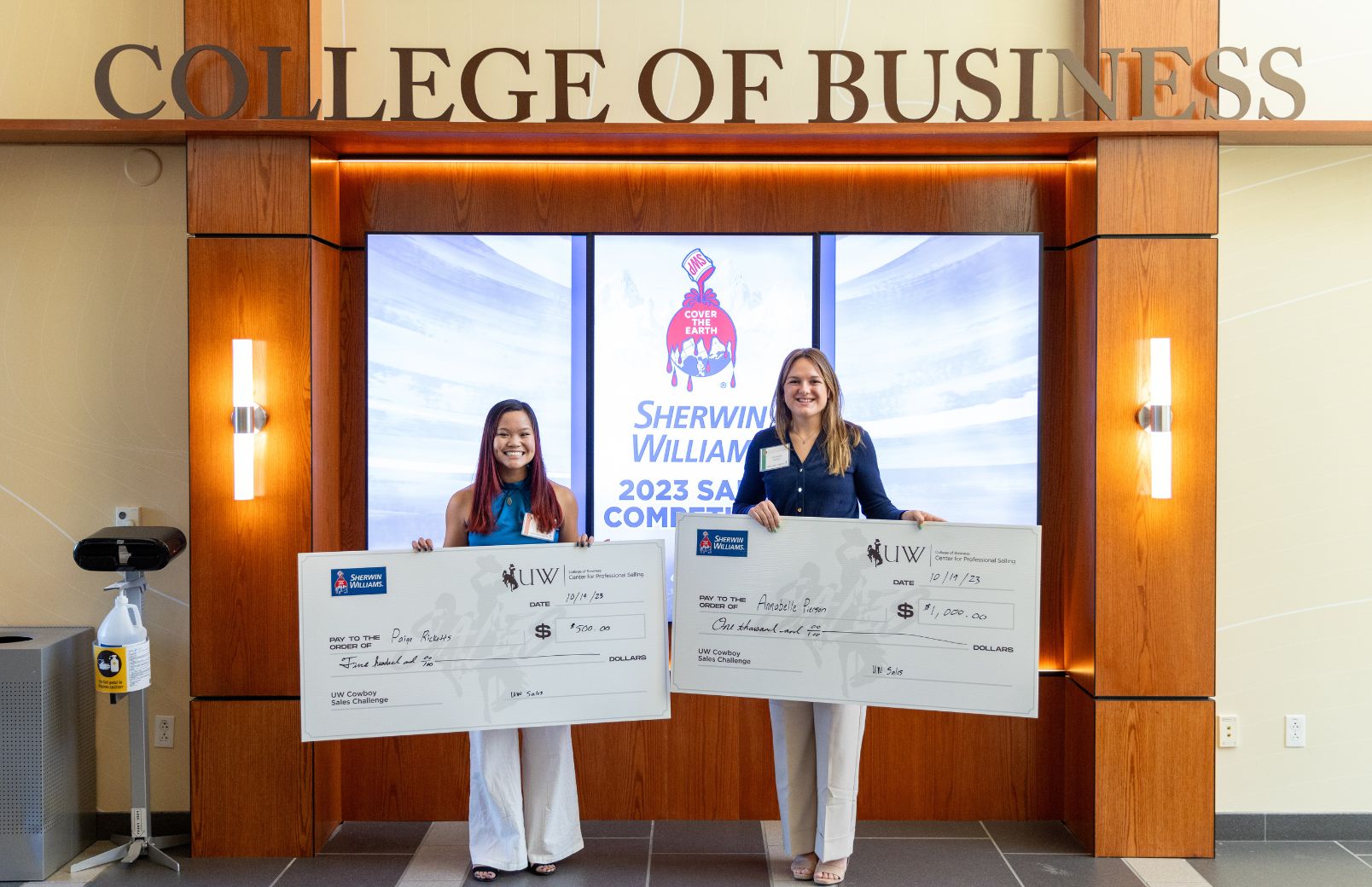 Students posing with their large checks in the College of Business after winning a sales competition