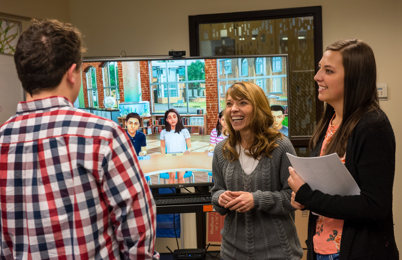 Professor and students talk in front of a classroom simulation