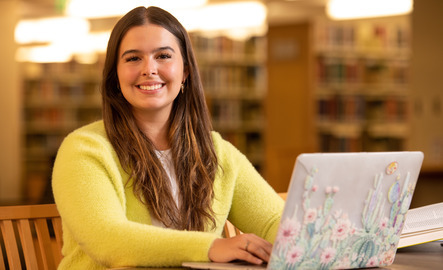 A student smiles for a photo while typing on their laptop