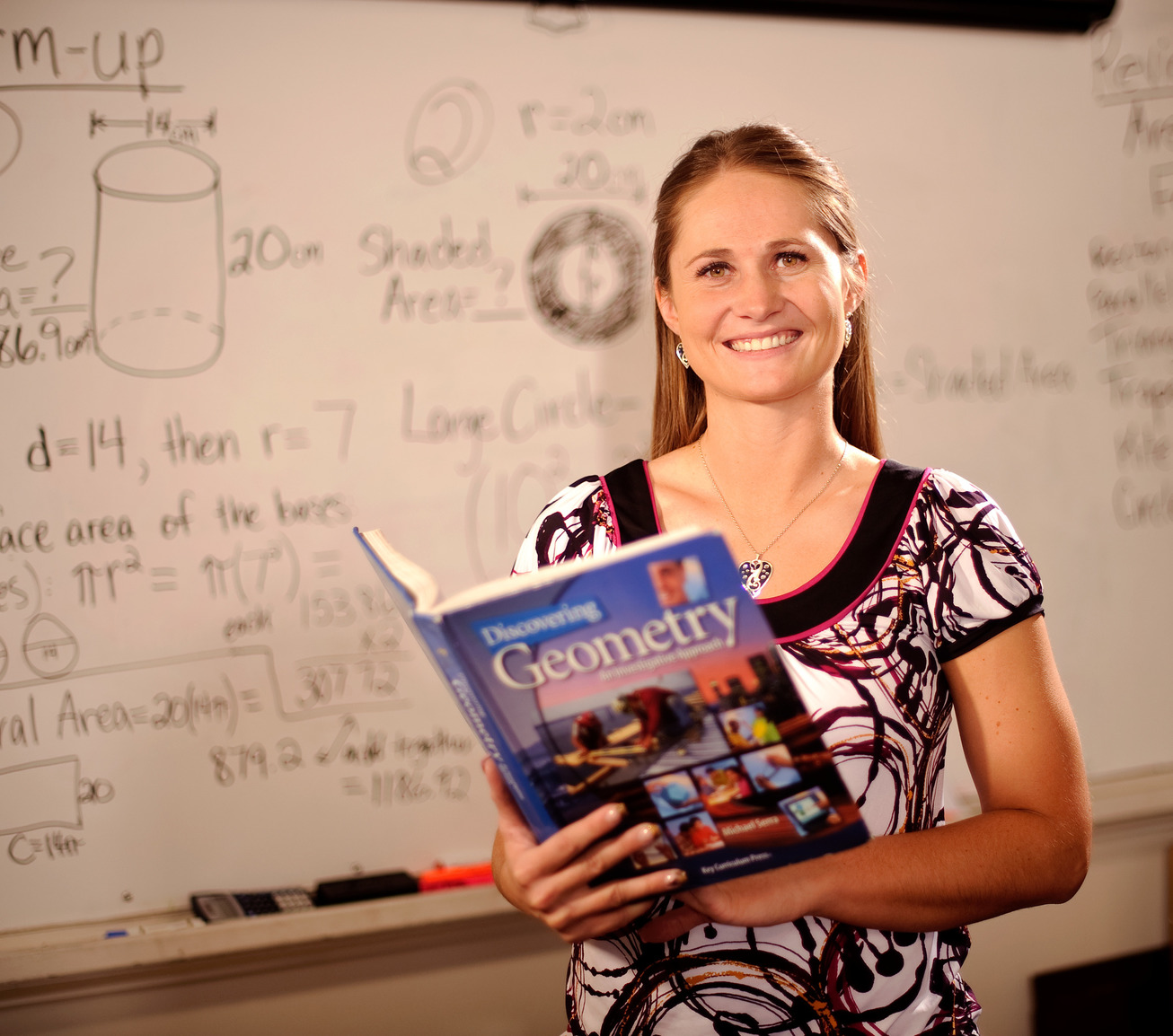 Teacher posing with geometry book in front of white board