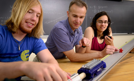 A professor helping two students with a science experiment