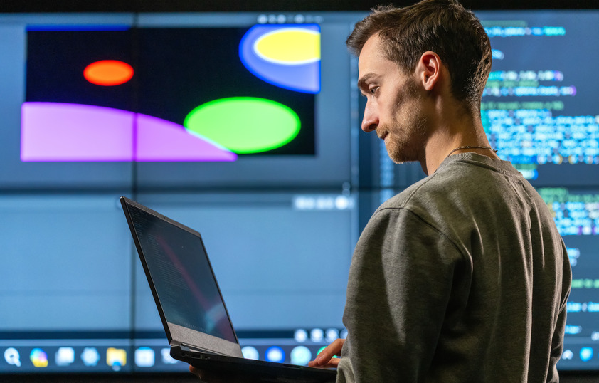 A student works on his laptop while standing in front of a projected software development project in the background