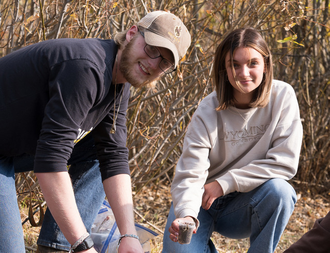 Two students collect a soil sample 