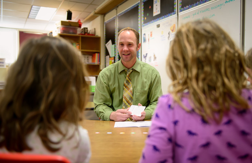 A teacher sits with two students at a table