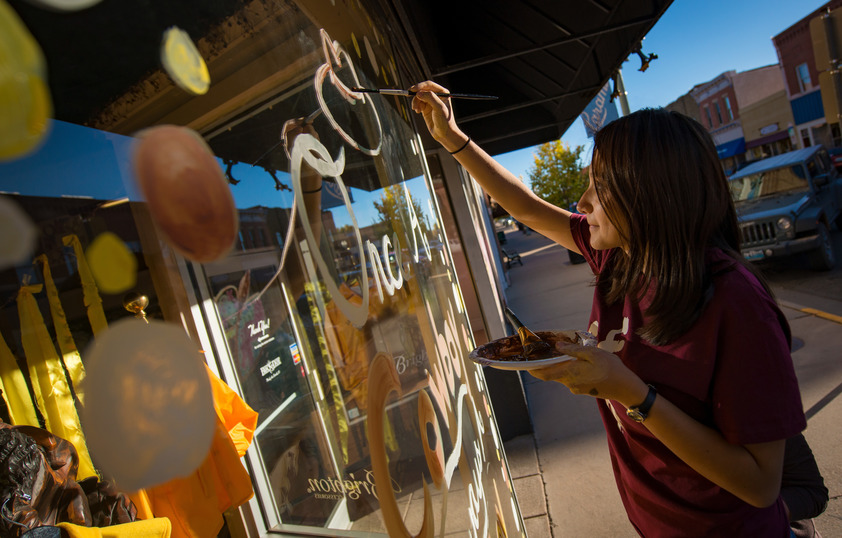 a student painting a downtown business front window