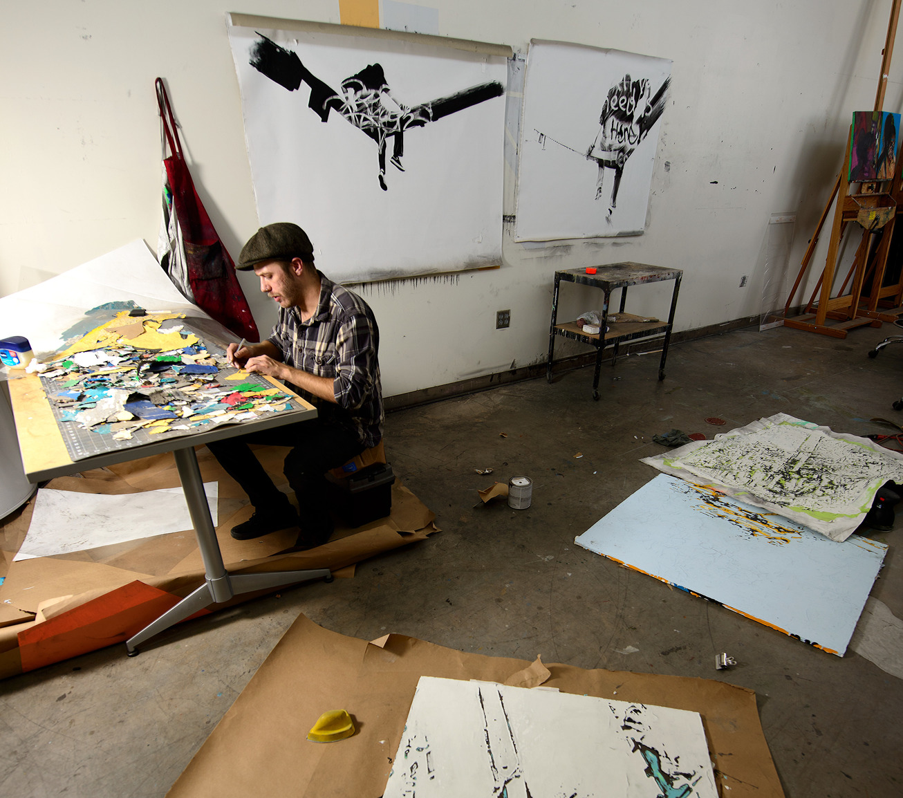 an artist working on a multimedia piece with completed works in the background