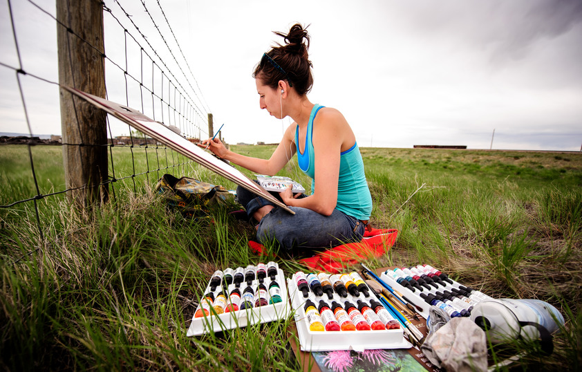 a student sitting in the grass outside and painting