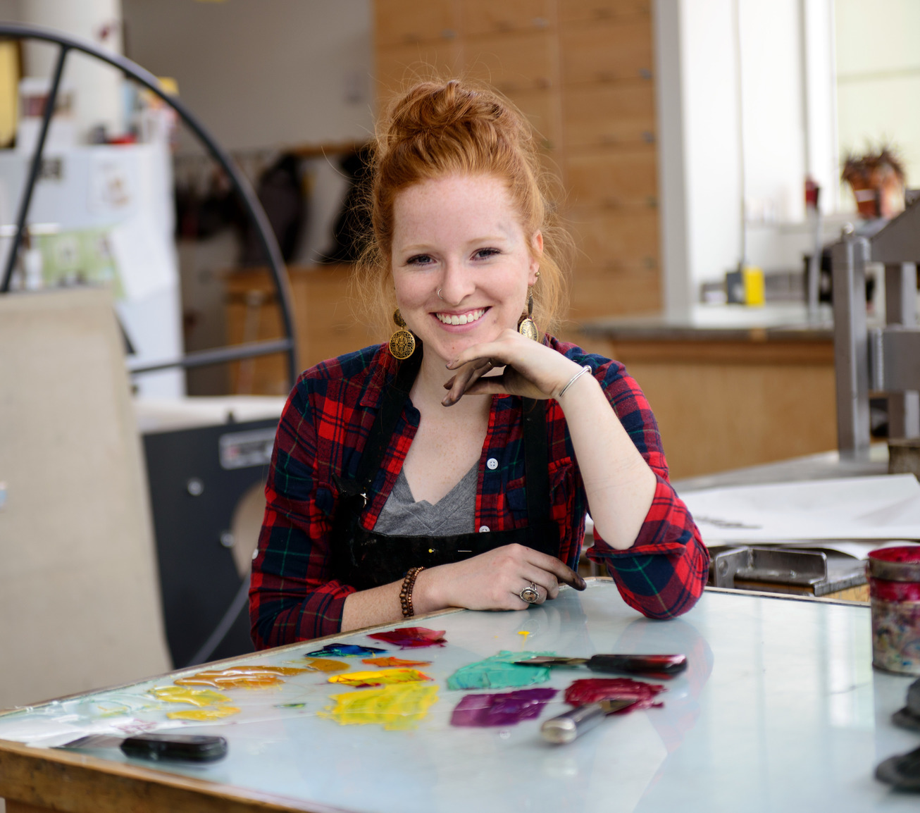 an artist with ink stained hands is smiling in front of a palette covered with different colors of printmaking inks