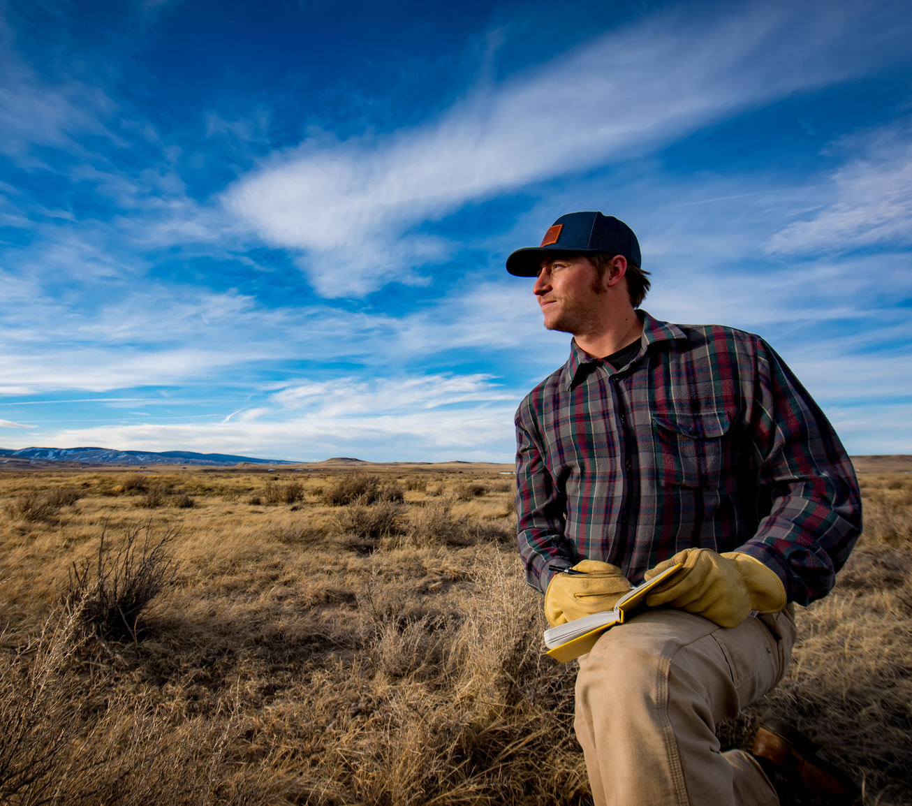 Student holds a pen and notepad in a dry field while looks off into the distance