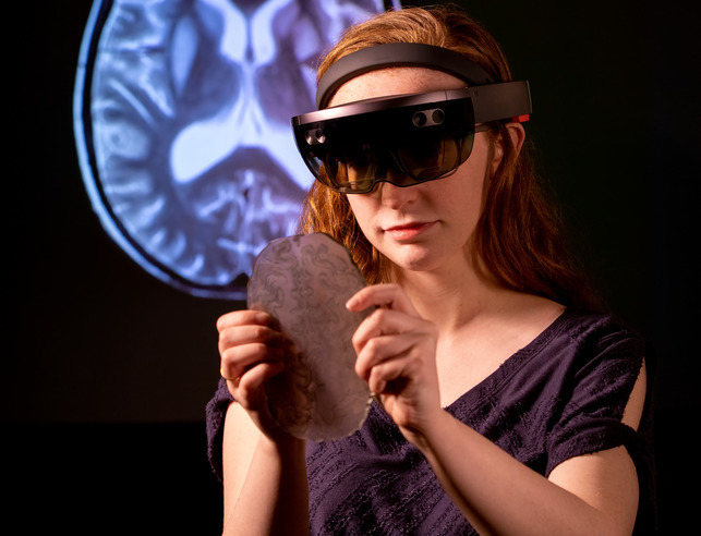 Student wearing virtual reality goggles looks at an image of a brain