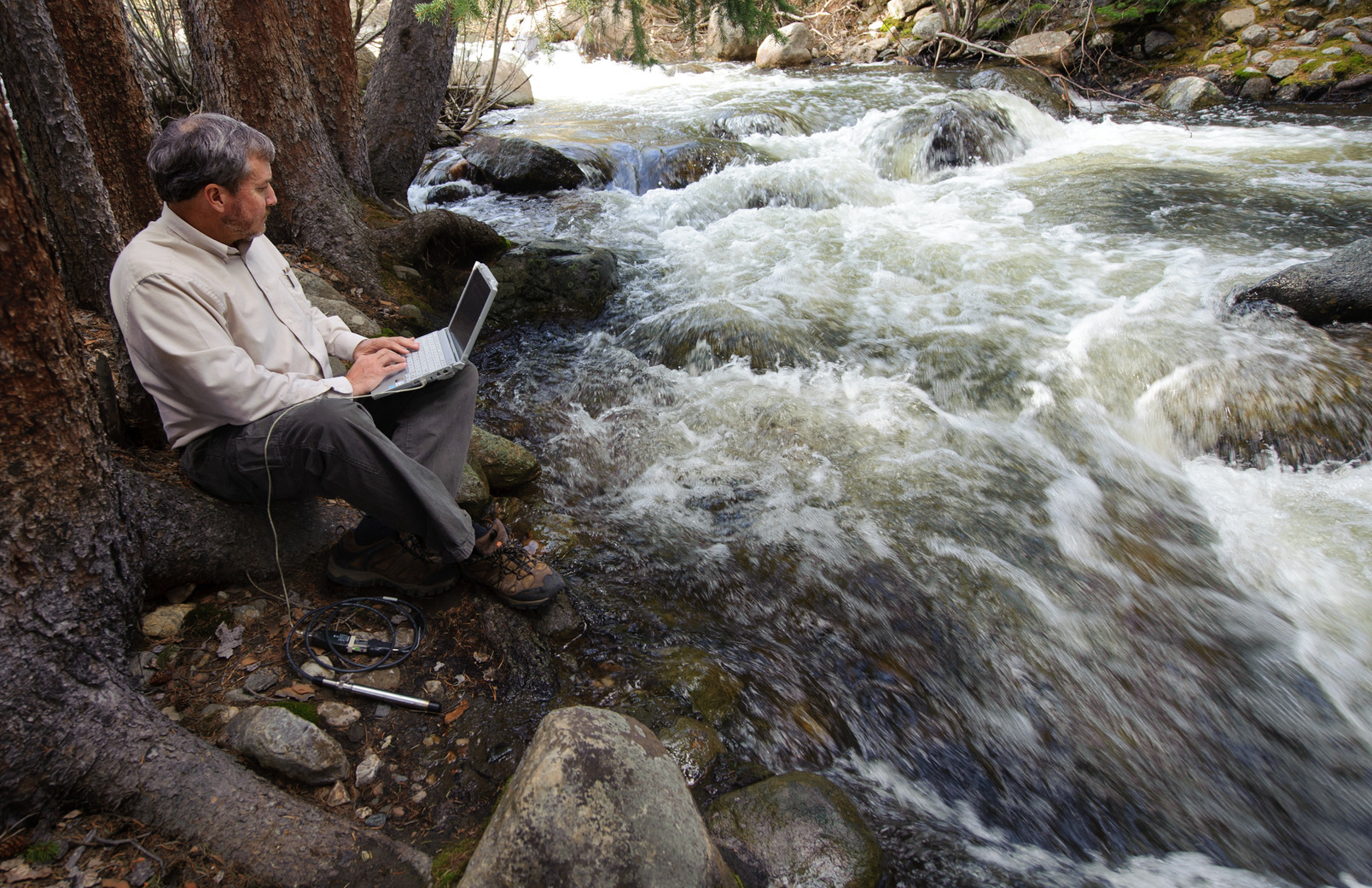 Researcher examining river with laptop in their lap