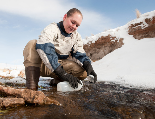 A student takes a water sample from a body of water