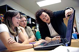 Three people conversing around computer